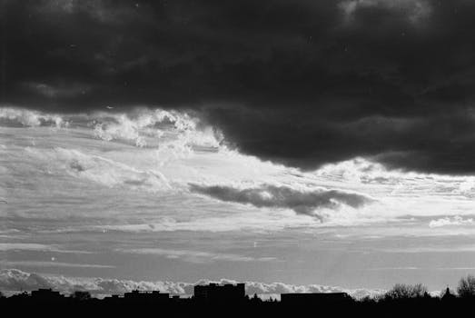 A dramatic black and white view of a cloudscape above a city skyline silhouette, exuding a moody atmosphere.
