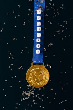 Gold medal on blue ribbon with 'Possible' beads on black confetti background.