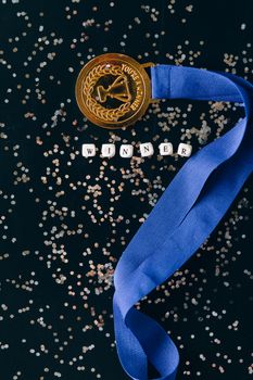 Close-up of a gold medal with blue ribbon on black surface with 'winner' text and glitter.