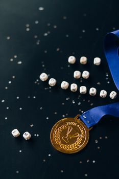 A gold medal with blue ribbon lies on a black surface surrounded by letter blocks forming the word 'impossible'.