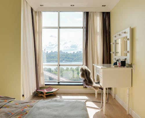 Interior of contemporary bedroom with large window with curtains and makeup mirror in daylight