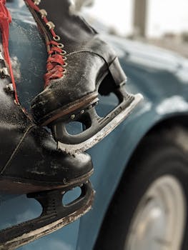 Close-up of vintage ice skates with red laces hanging on a classic car.