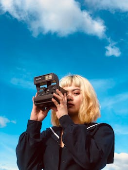 Blond woman with short hair using vintage camera against a bright blue sky
