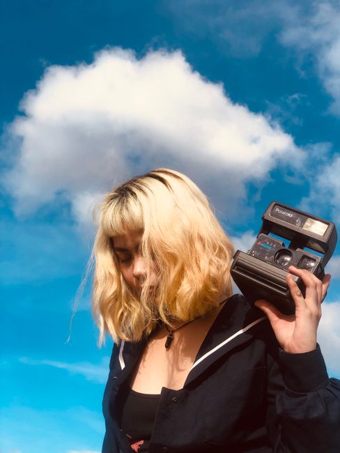 Young ethnic female standing with retro camera in hands in daytime under blue cloudy sky