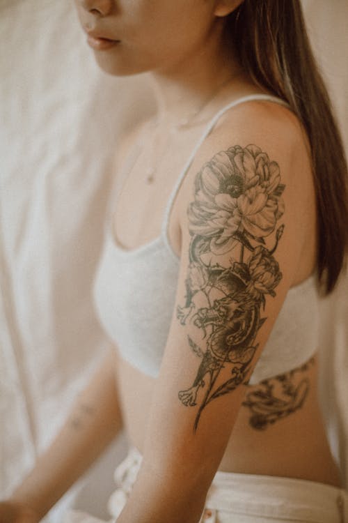 Side view of crop anonymous female with tattoo in lingerie resting in room with white fabric