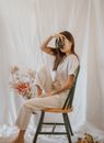 Side view of slender anonymous female in casual outfit with old photo camera resting on chair among gentle flowers