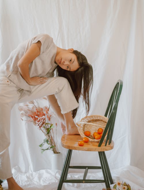 Gentle Asian woman leaning on chair with basket of mandarins