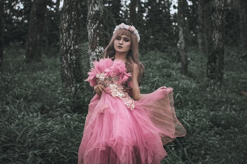 Beautiful woman in chiffon pink dress standing in summer forest
