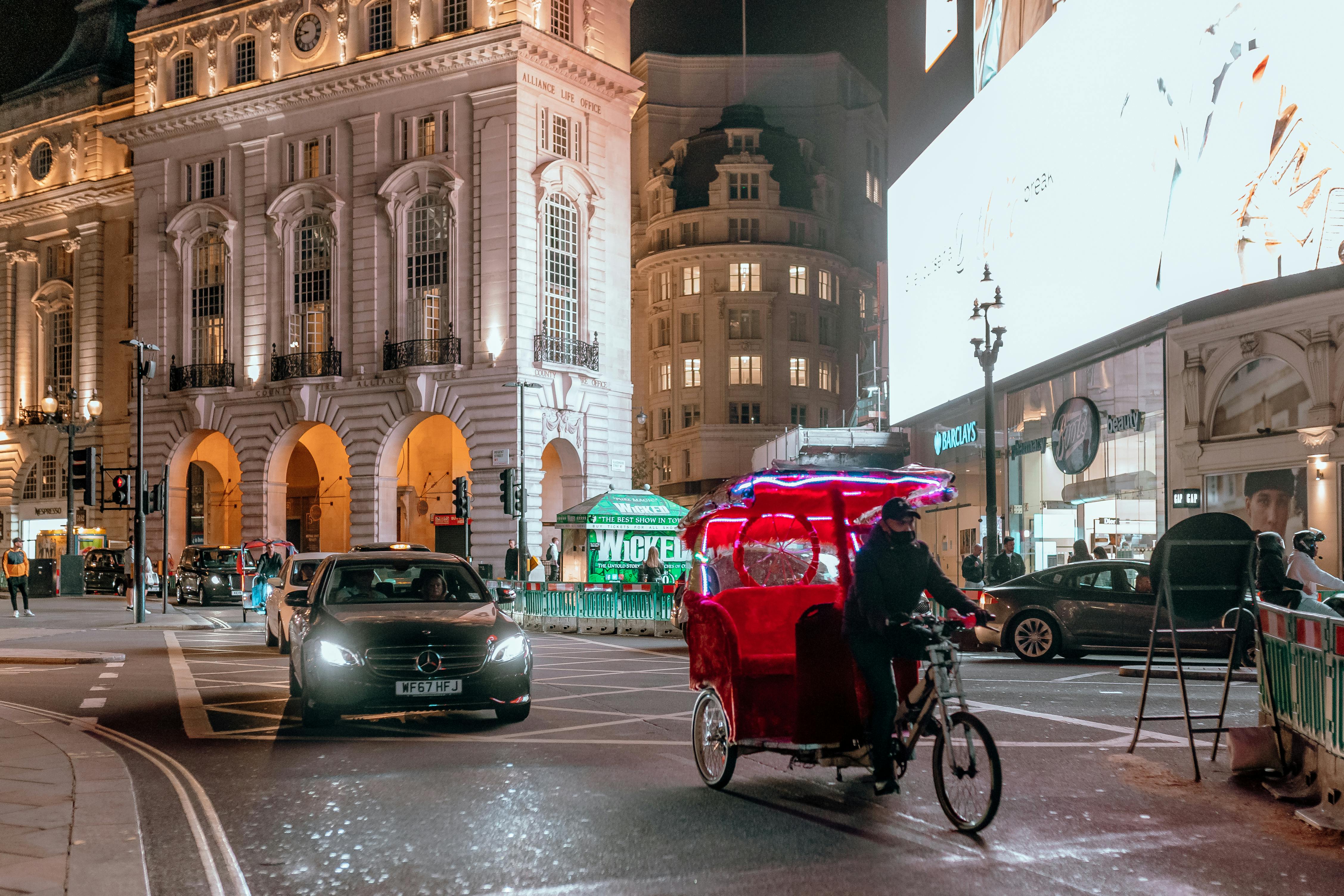 A lively evening scene in London's city center, showcasing a rickshaw and illuminated architecture.
