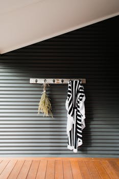 A striped bathrobe and decorative twigs hanging on a rustic wooden hook inside a modern bathroom.