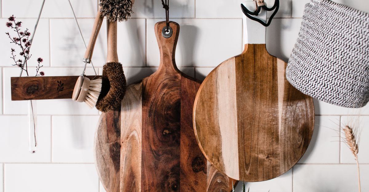 Iemand reinigt een houten snijplank met een zachte spons bij de gootsteen.