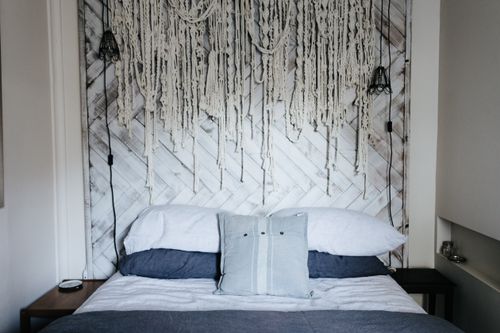 Free Cozy bedroom interior featuring a unique hanging decoration on a wooden headboard. Stock Photo