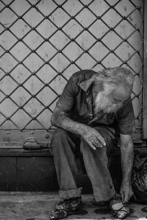 Homeless man sitting near metal fence on street