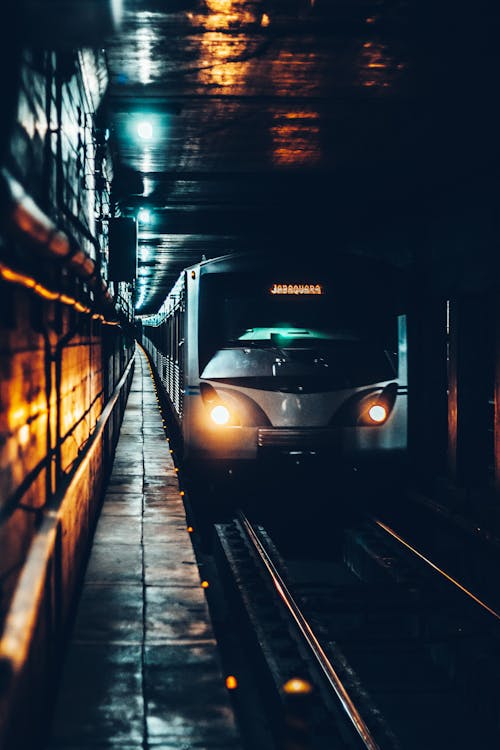 Modern electric train with glowing headlights riding on railway and approaching underground station