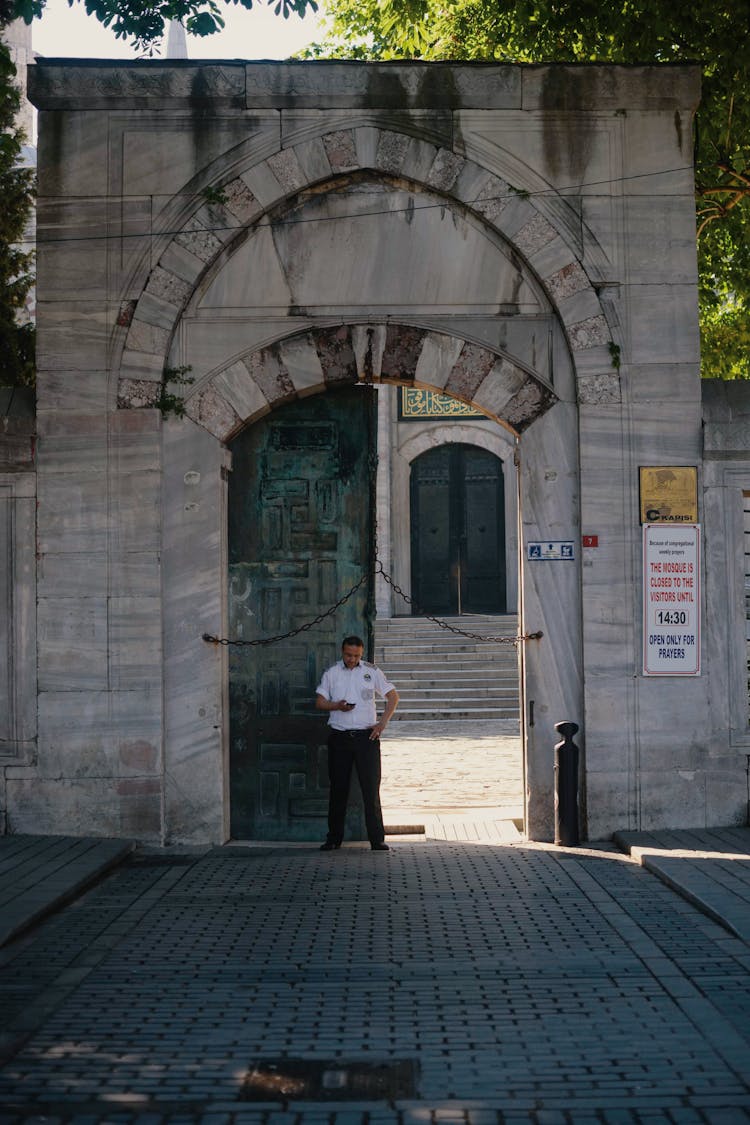 Security Guard Standing At Arched Gates Of Historic Building