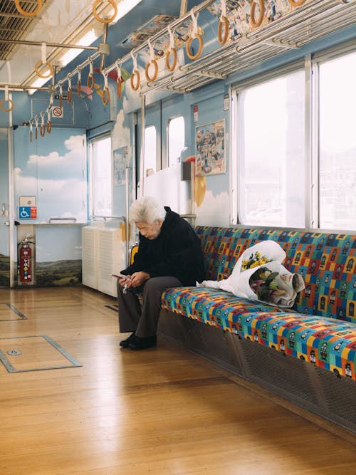 Full body of senior ethnic male watching cellphone while sitting with bunch of flowers in wagon of metro