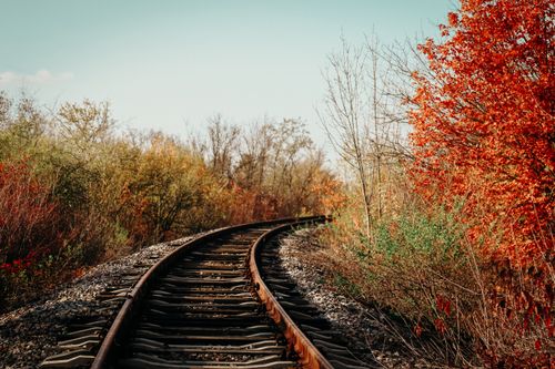 Free Curved railway tracks surrounded by vibrant autumn foliage and clear blue sky. Stock Photo