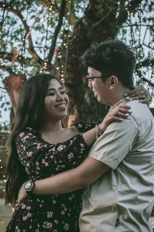 Free A couple embraces and smiles warmly under string lights against a natural backdrop. Stock Photo