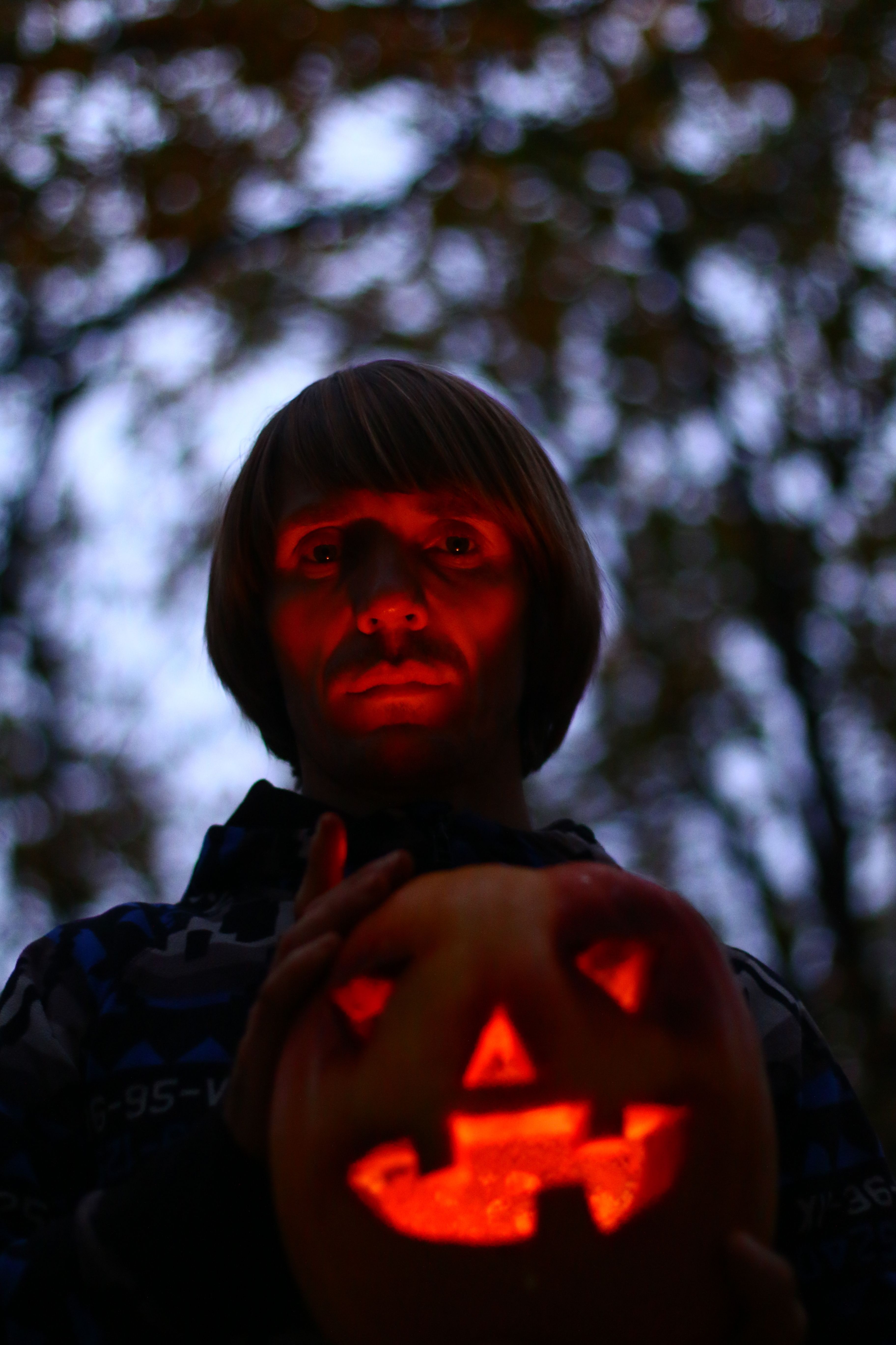 Spooky portrait of a person holding a glowing Jack-O'-Lantern outdoors at dusk.
