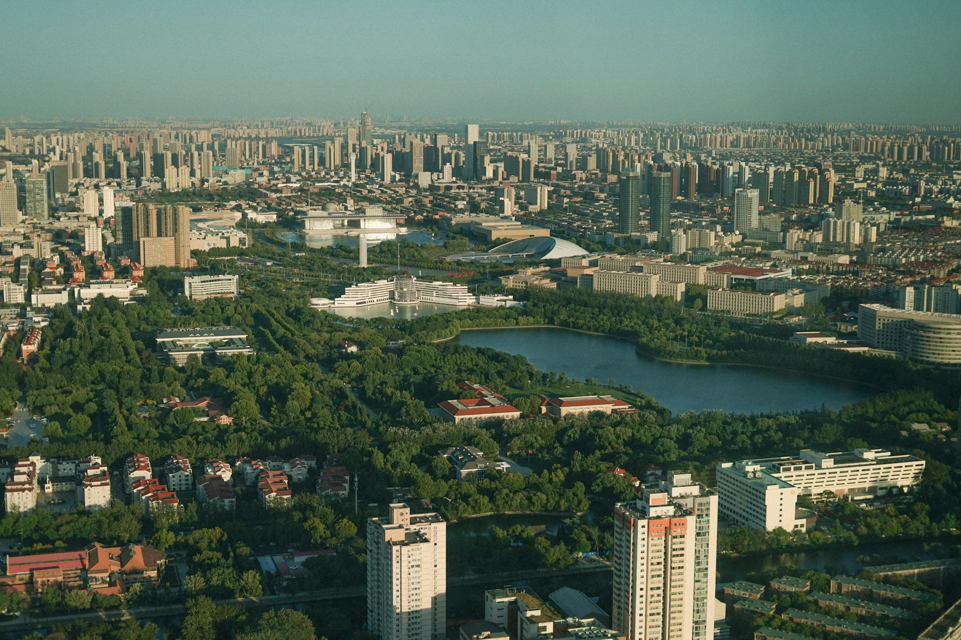 Aerial view of an expansive cityscape featuring skyscrapers, greenery, and a central lake, showcasing urban and natural harmony.