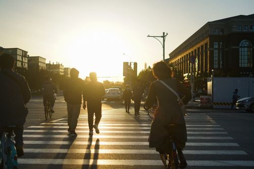 Free Silhouetted commuters cross the street at sunset, creating dynamic shadows in the cityscape. Stock Photo