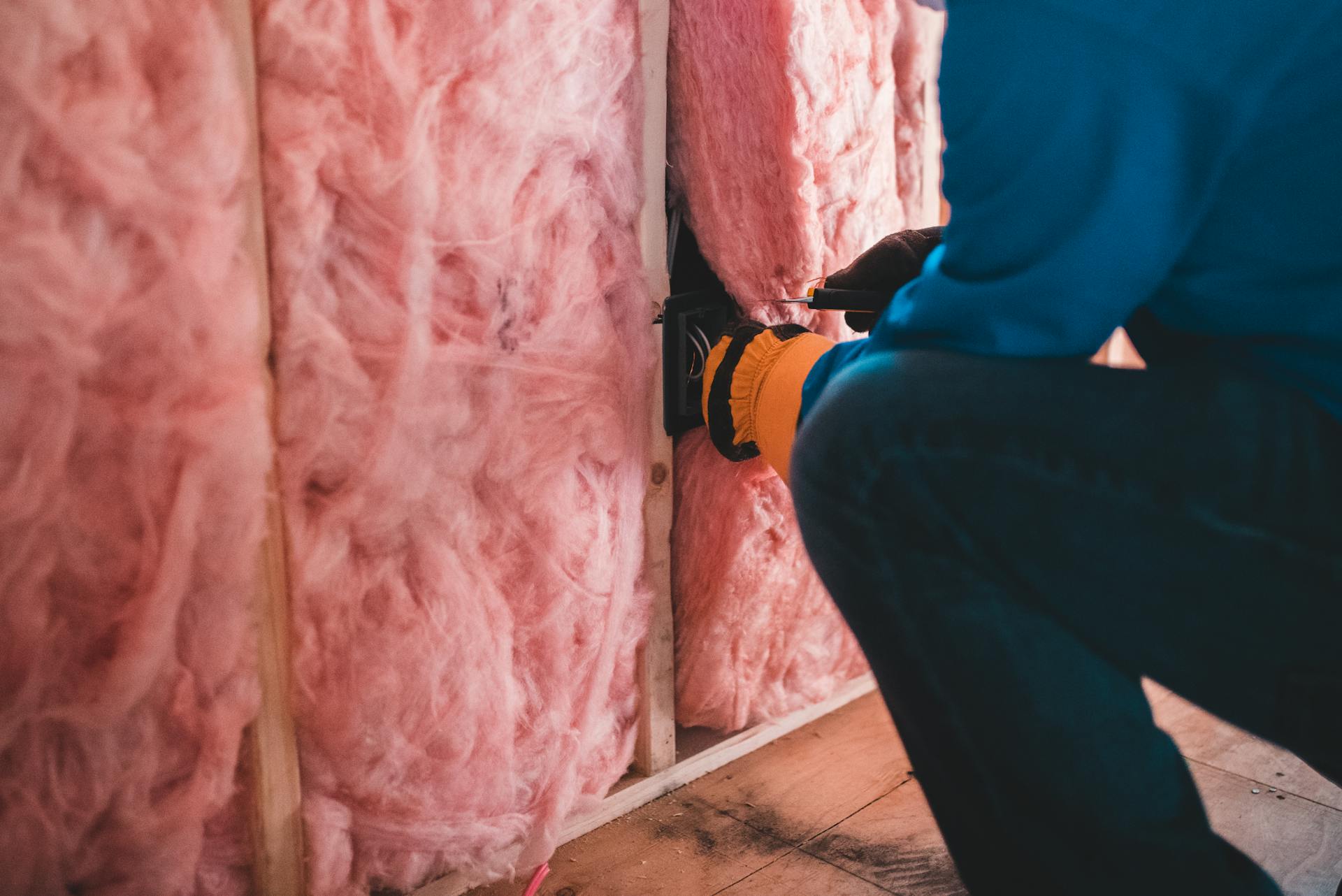 Focused worker installing pink fiberglass insulation in a building interior.