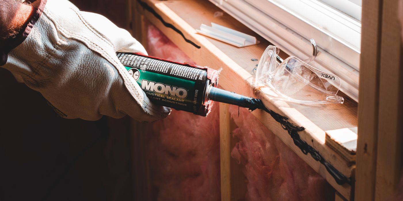A gloved hand running a caulk gun along a seam