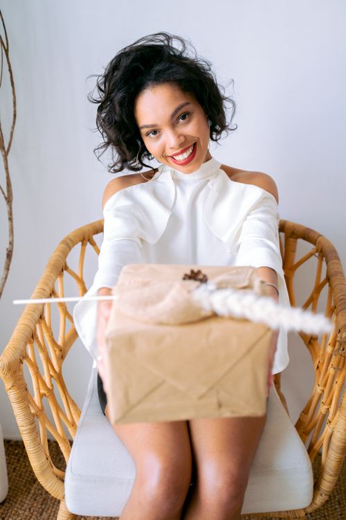 Free Happy woman sitting and presenting a wrapped gift, creating a joyful and warm atmosphere. Stock Photo