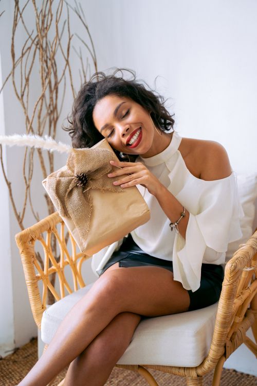 Free Smiling woman sits indoors, embracing a beautifully wrapped present with joy. Stock Photo