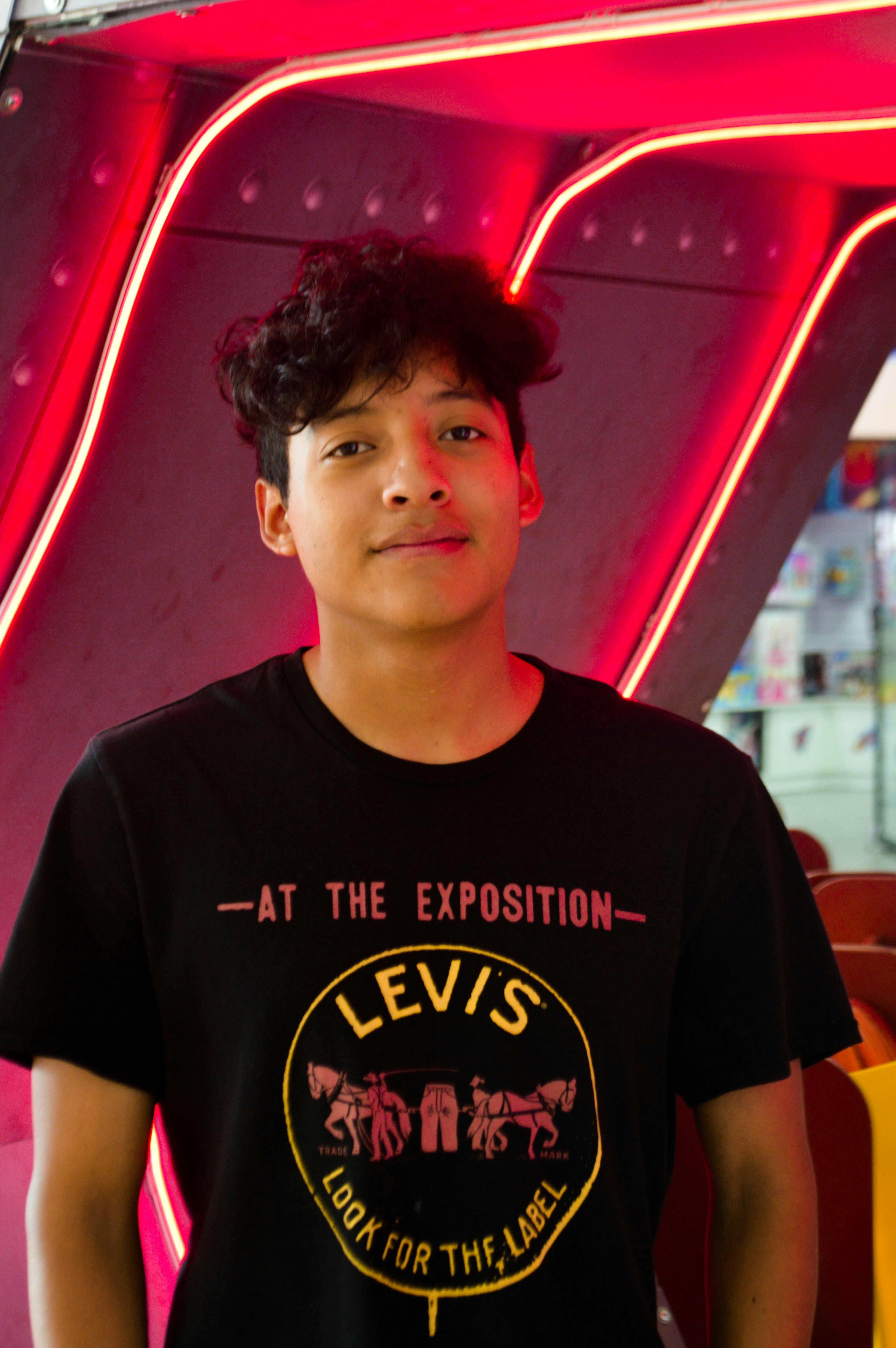 Portrait of a young man standing indoors with neon red lighting, exuding modern style.