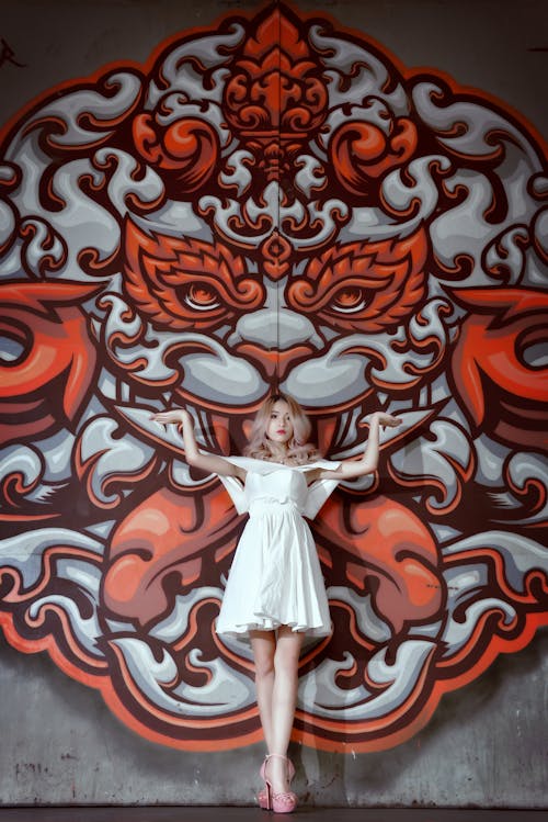 Woman in White Dress Standing on Red and White Floral Wall