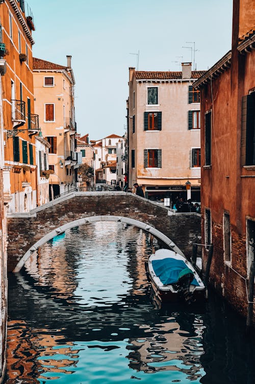 A Boat Under A Concrete Bridge Between Brown Buildings