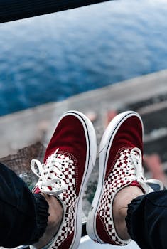 Person wearing red checkered sneakers sitting above a view of the ocean.