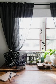 A home workspace featuring baskets, plants, and a wooden table by a sunlit window, offering a cozy atmosphere.