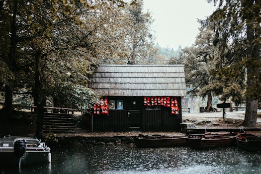 A scenic lakeside cabin surrounded by trees and moored wooden boats in a serene, rainy landscape.