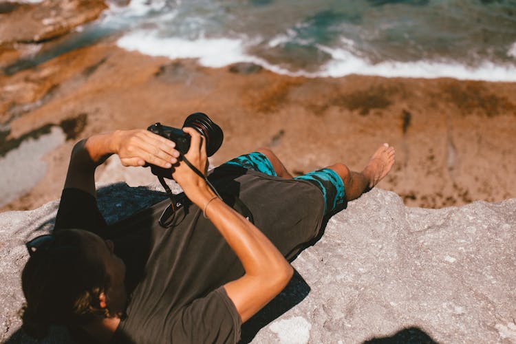 A Photographer Lying On Edge Of A Rock Cliff Taking Photo