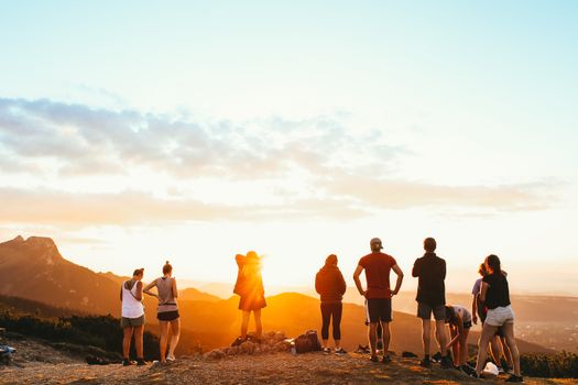 A group of friends watching a beautiful sunset on a mountain, symbolizing adventure and unity.