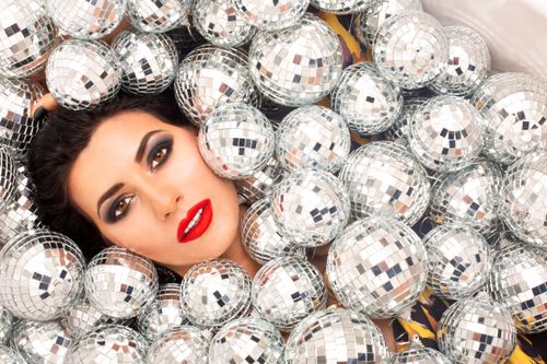Free Top view of pretty female with makeup looking at camera while lying amidst small shining silver disco balls during holiday Stock Photo