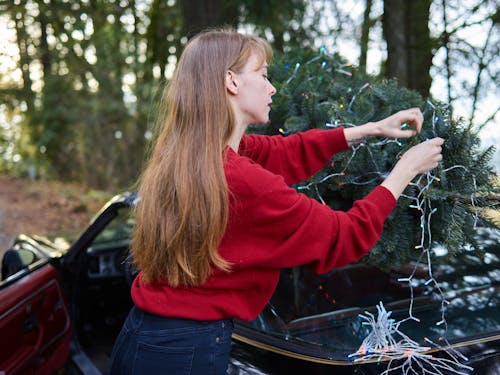 Woman in Red Long Sleeve Shirt Decorating a Christmas Tree