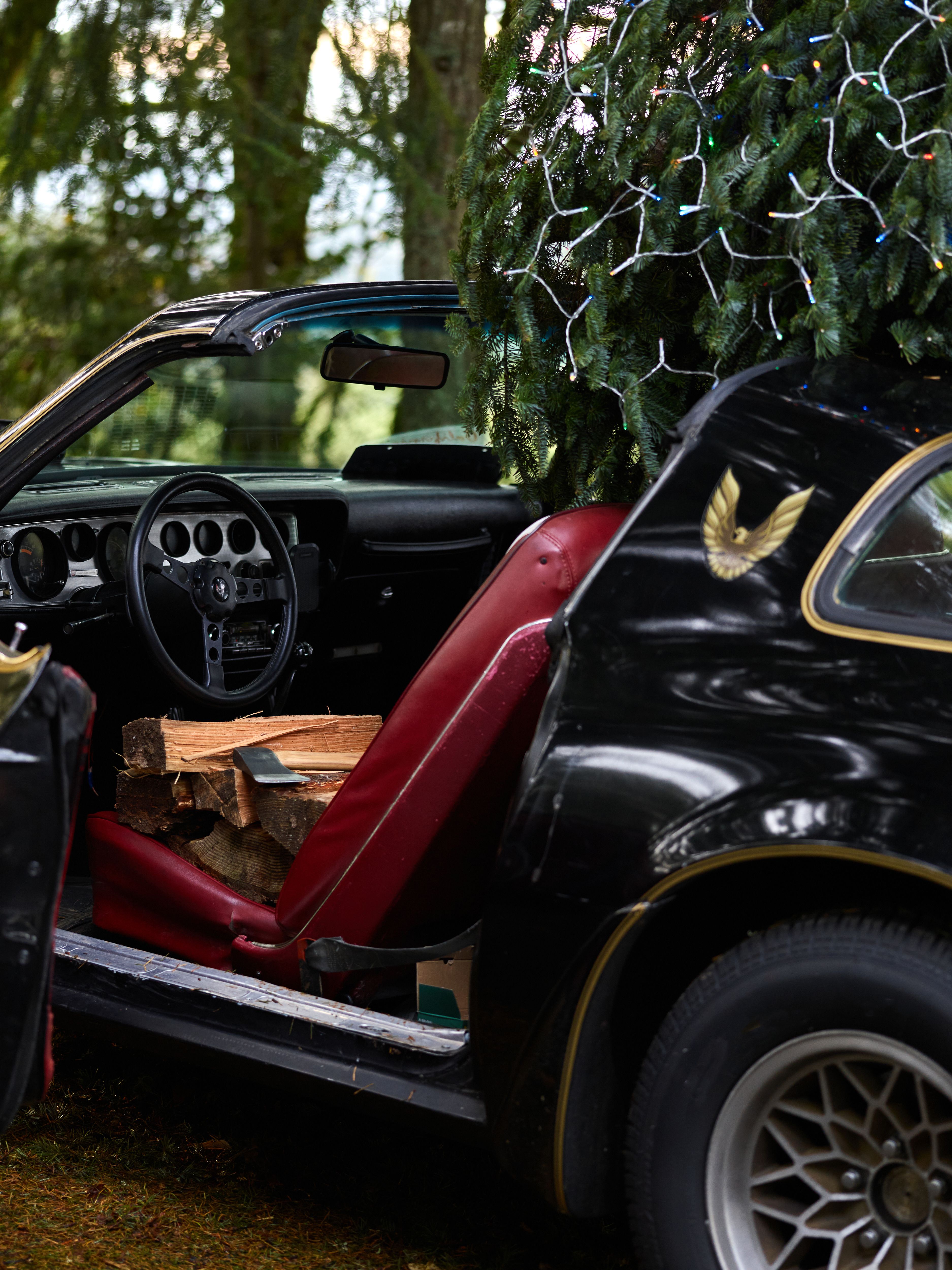 A classic black car with a Christmas tree and wood logs inside, captured outdoors.