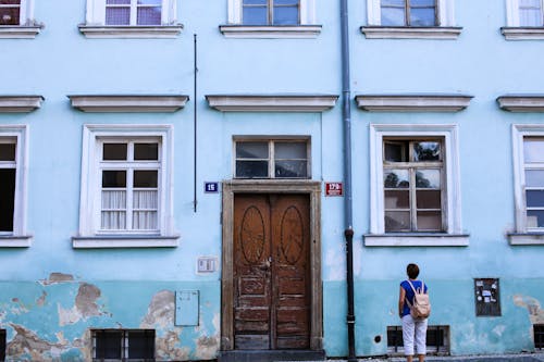Free Person in Blue Shirt and White Pants Standing beside the Building Stock Photo
