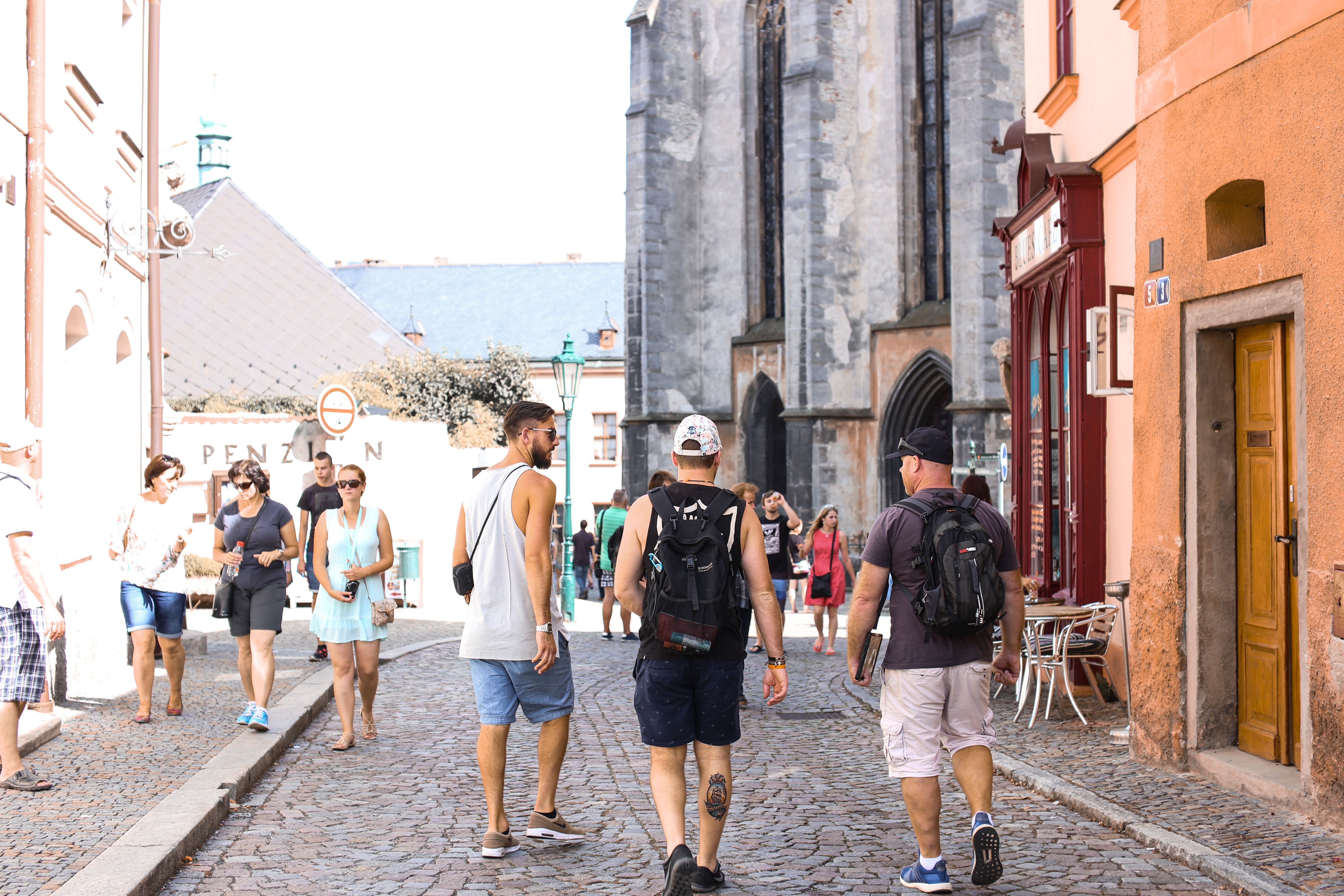 Tourists walk along a historic cobbled street lined with old buildings and a church in the background