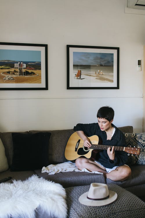 A Woman Playing the Guitar while Sitting on a Couch