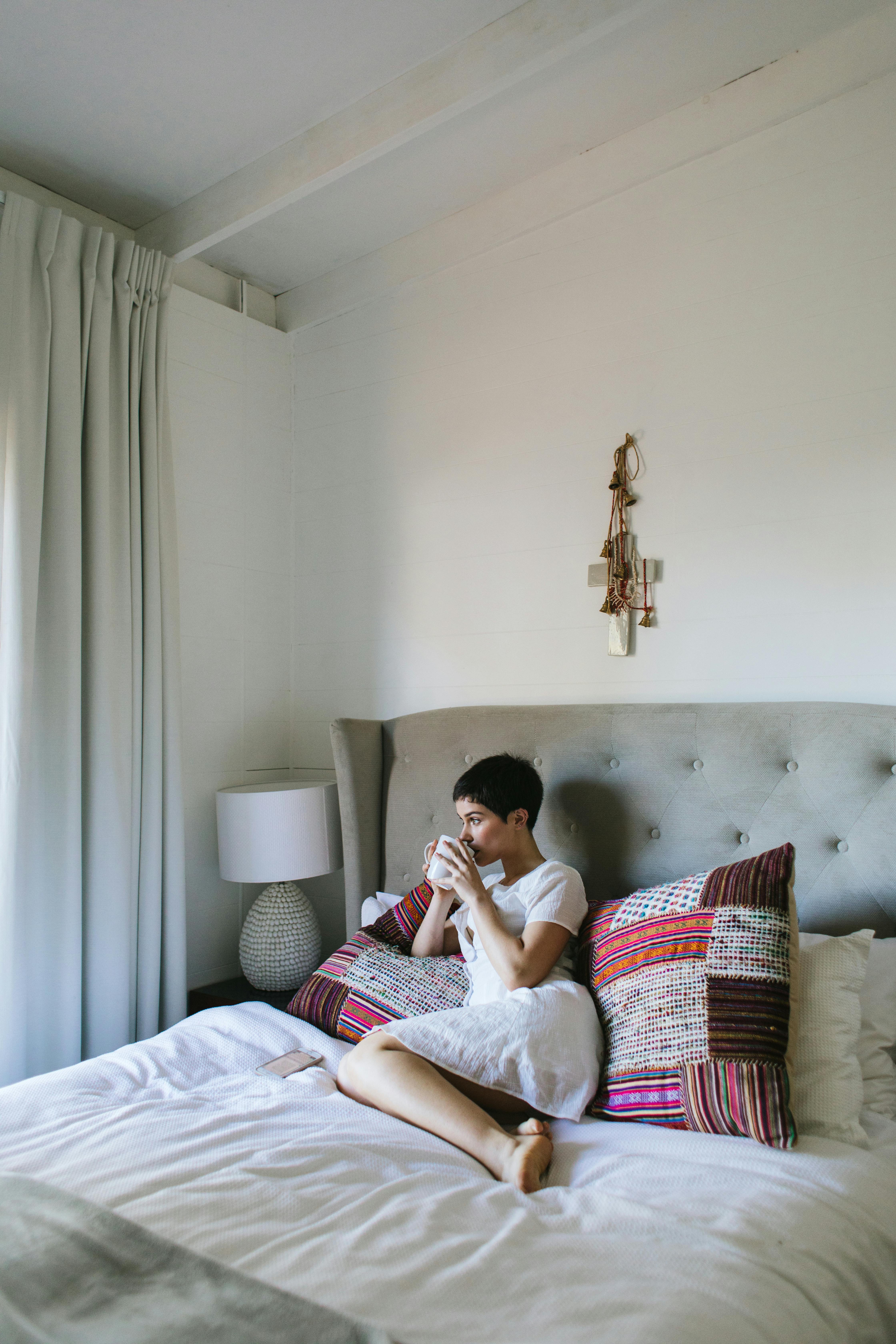 Woman drinking coffee in a cozy, modern bedroom with natural light.