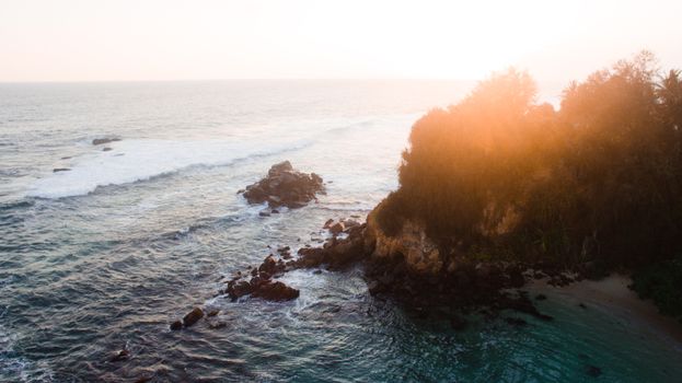A breathtaking aerial view of a rocky coastline at sunset, showcasing the natural beauty of the sea and shore.
