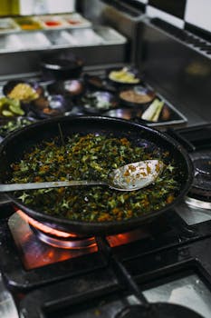 Close-up of herbs being cooked in a pan on a stove in a kitchen setting.