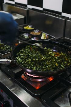 A chef cooking delicious vegetable dish with fresh herbs and spices on a stove.
