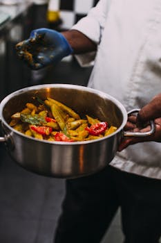 A chef mixing vibrant vegetables in a stainless steel pot in a professional kitchen.