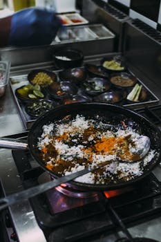 Focused shot of a frying pan with ingredients, spices, and herbs in a restaurant kitchen setting.