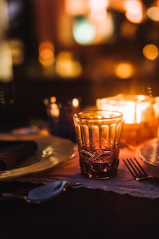 A cozy dining setting illuminated by candlelight, featuring an ornate glass and elegant tableware.